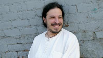 Leon Santiago, wearing a white shirt and white pants, leans back against a white brick wall.