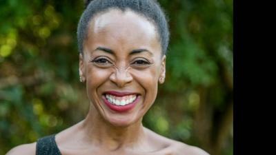 A woman smiles brightly at the camera, her hair pulled back in a ponytail