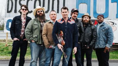 seven men standing in jeans and shirts and cowboy hats looking at the camera