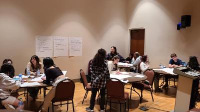 Students work around tables, talking and making notes about a project
