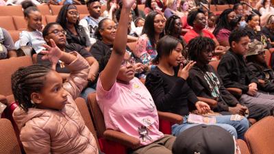 students in theatre seats with one raising their hand