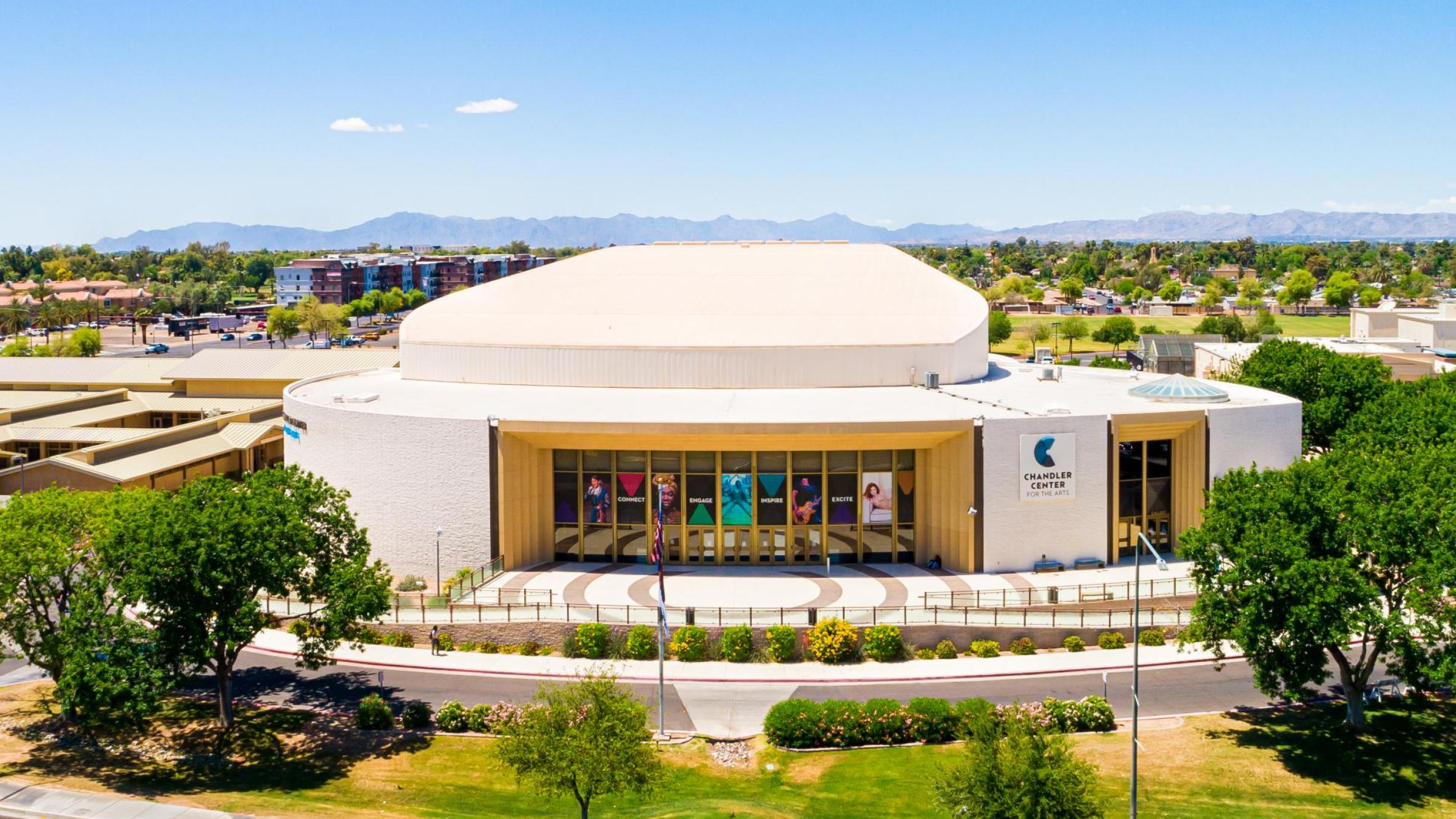 The CCA performing arts building with trees on either side, grass in front and a blue sky above. 