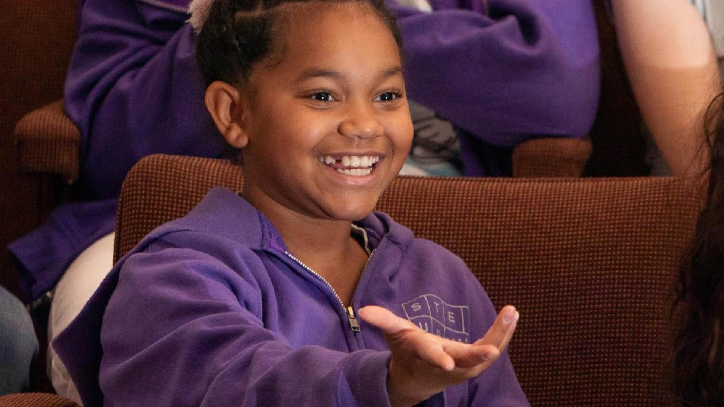 Two young girls sit in theatre seats, enjoying a show