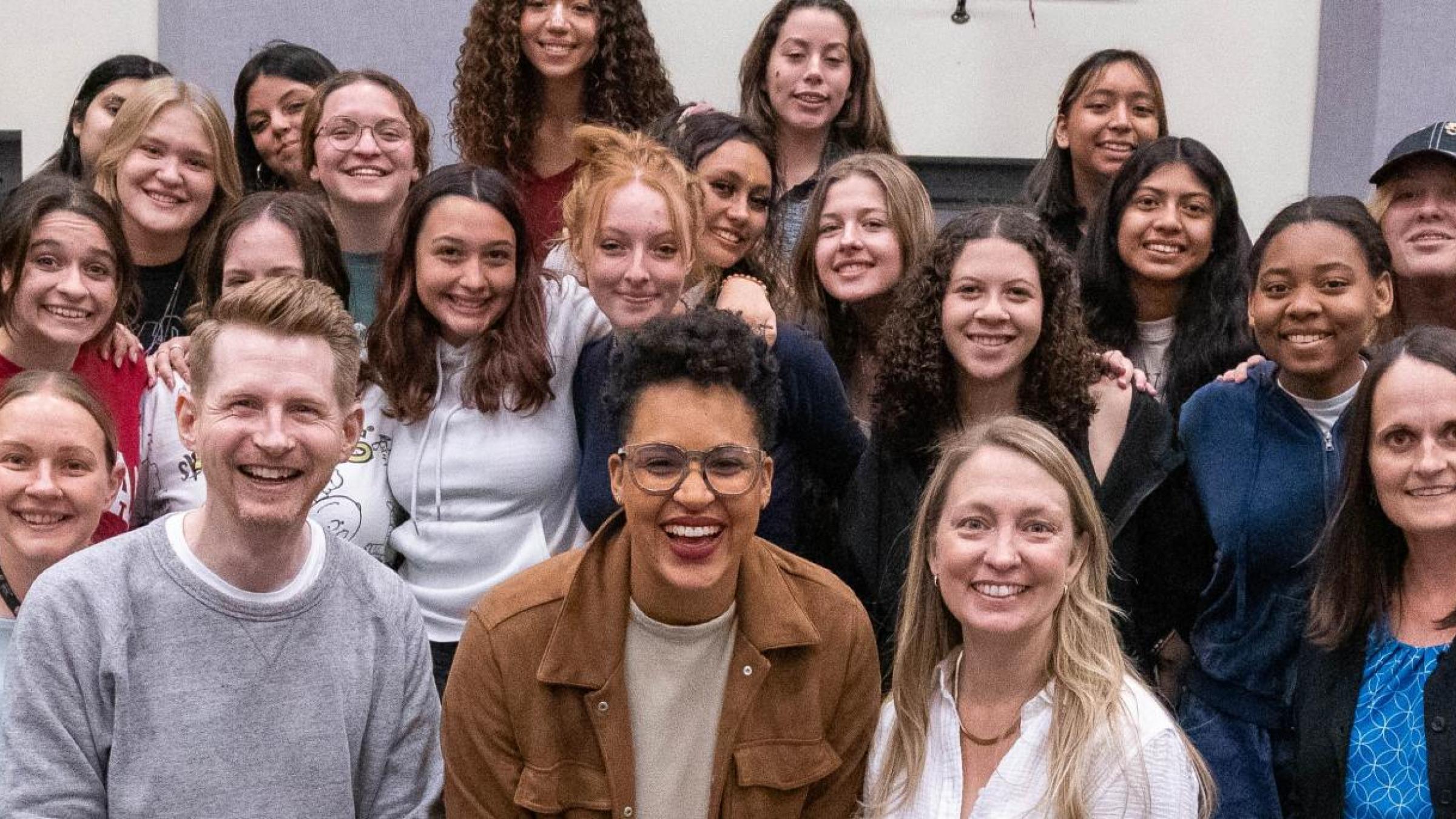 A group of students and teachers smile at the camera from risers